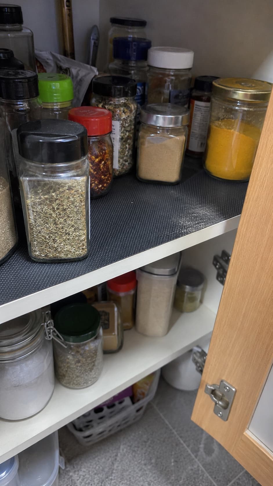 Black liner beneath closed spice jars in an everyday cupboard.
